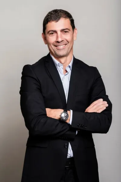 Homme souriant en costume noir, bras croisés, portant une montre.