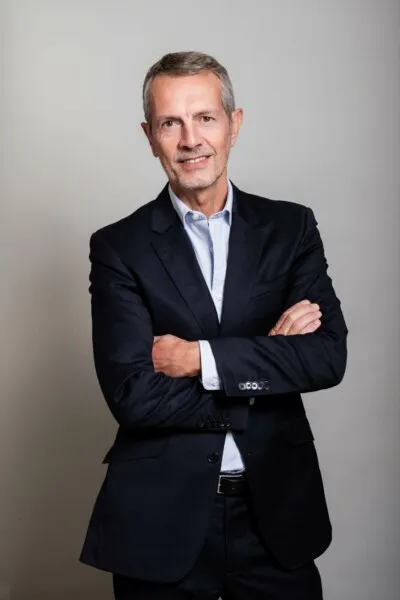 Homme d'affaires souriant en costume bleu marine, bras croisés, regardant la caméra.