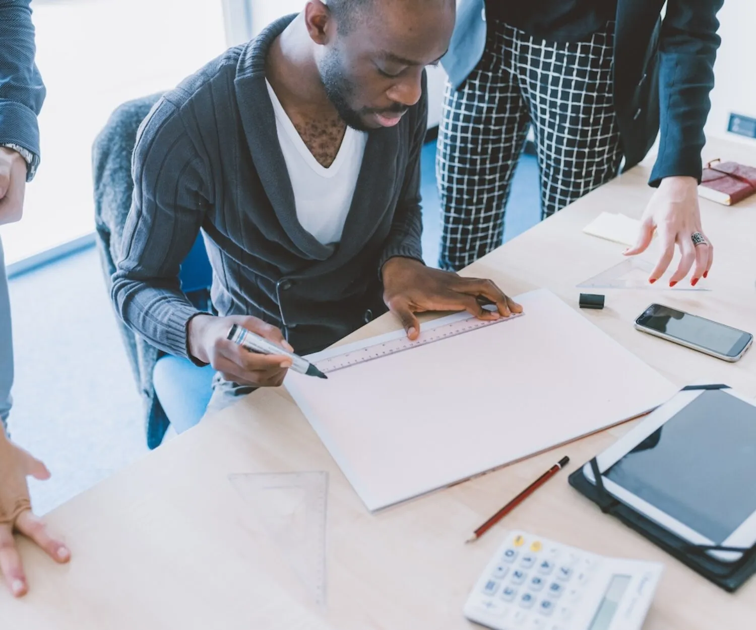 Homme dessinant un plan avec une règle et un marqueur lors d'une réunion d'équipe.
